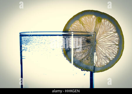 Getränke und Erfrischungen Konzept - Glas Mineralwasser mit Zitronenscheiben auf reflektierende Oberfläche Stockfoto
