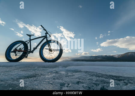 Fatbike (auch genannt fat-Bike oder mit dem Fett-Reifen Fahrrad) - Radfahren auf großen Rädern. Fahrradständer vor dem Hintergrund des Sonnenuntergangs auf dem Eis. Stockfoto
