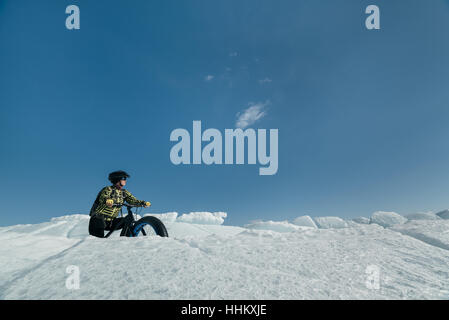Fatbike (auch genannt fat-Bike oder mit dem Fett-Reifen Fahrrad) - Radfahren auf großen Rädern. Extreme Mädchen Fahrrad fahren auf Schnee geschmolzen Eis. Der Baikalsee. Stockfoto
