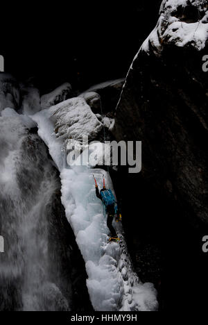 Kletterer auf vereisten Felsen neben teilweise gefrorenen Wasserfall aufsteigend Stockfoto