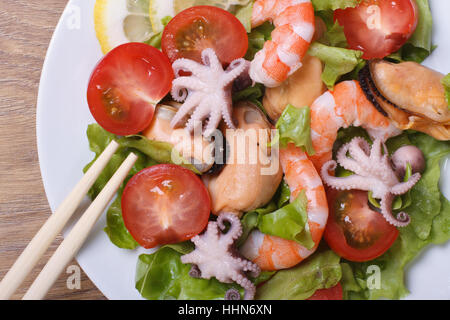 Salat mit Garnelen, Muscheln, Tintenfisch mit Gemüse hautnah auf einem Teller mit Stäbchen. Ansicht von oben Stockfoto