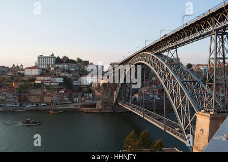 Portugal: Boote bei Sonnenuntergang und die Skyline von Porto mit Blick auf die Luiz I, die Doppel-gedeckten Metall Bogenbrücke über den Fluss Douro Stockfoto