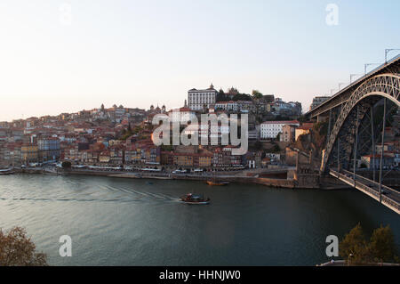 Portugal: Boote bei Sonnenuntergang und die Skyline von Porto mit Blick auf die Luiz I, die Doppel-gedeckten Metall Bogenbrücke über den Fluss Douro Stockfoto