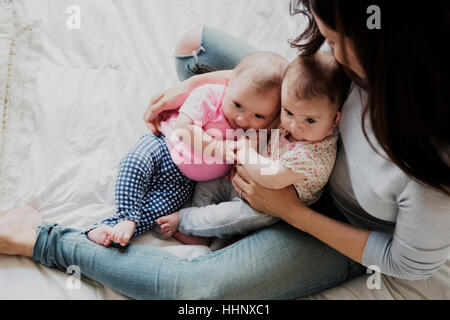 Kaukasische Mutter sitzt auf Bett halten Baby Zwillingstöchter Stockfoto