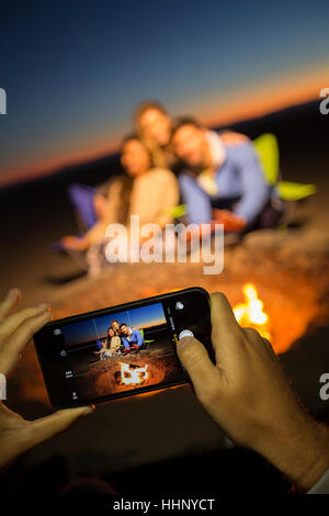 Hände von Frau fotografieren Freunde am Strand mit Handy Stockfoto