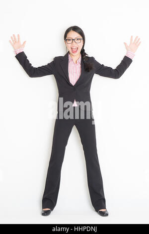 Voller Länge Vorderansicht des schockiert junge asiatische Geschäftsfrau in festlich gekleidet, stützte sich auf Wand, stehend auf einfarbigen Hintergrund. Stockfoto