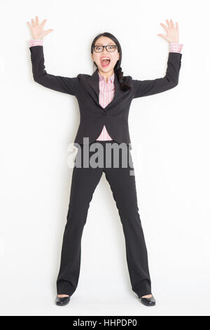 Voller Länge Vorderansicht des schockiert junge asiatische Geschäftsfrau in festlich gekleidet Bang und stützte sich auf Wand, stehend auf einfarbigen Hintergrund. Stockfoto