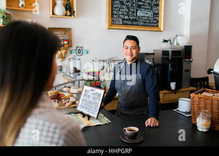 Kunde erhält ihren Kaffee aus einer lächelnden hispanische barista Stockfoto