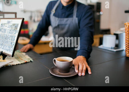 Barista eine frisch gebrühte Tasse Kaffee an einem Kunden übergeben. Stockfoto
