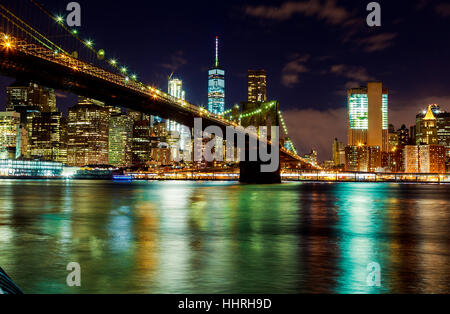 Brooklyn Bridge über den East River in New York City Manhattan nachts mit Licht und Reflexionen. Stockfoto