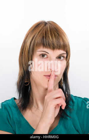 Kopfporträt einer jungen Brünette Frau vor weißem Hintergrund ist Legende den Finger auf den Mund. Stockfoto