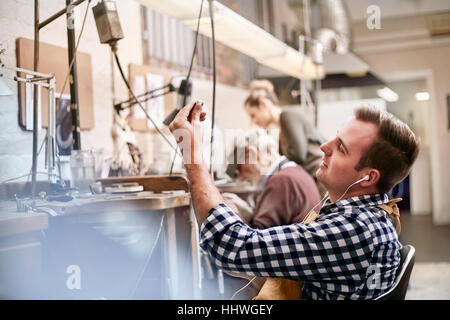 Männliche Juwelier Musikhören mit Kopfhörer in Werkstatt Stockfoto