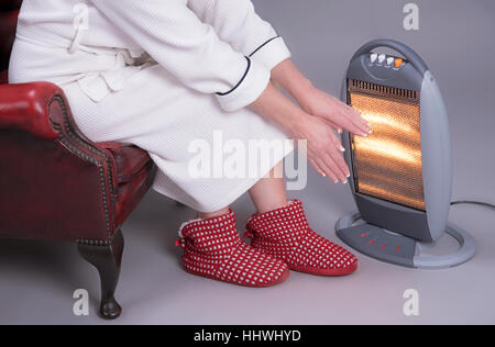 Frau im Morgenmantel Erwärmung ihre Hände vor ein elektrischer Kamin warm zu halten Stockfoto