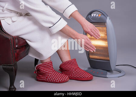 Frau im Morgenmantel Erwärmung ihre Hände vor ein elektrischer Kamin warm zu halten Stockfoto