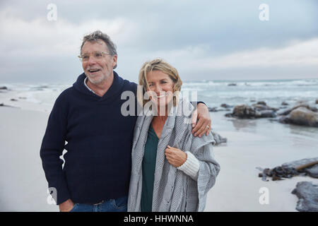 Porträt, Lächeln, älteres paar umarmt am stürmischen Strand Stockfoto