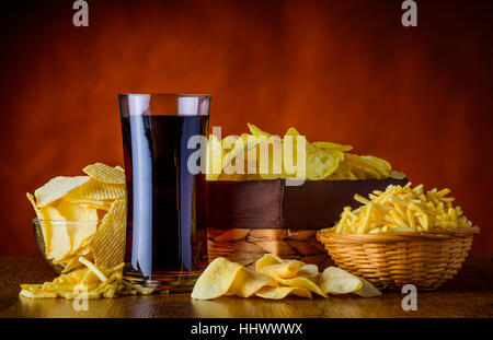 Verschiedene Arten von Kartoffel-Snacks und ein Glas Cola, ungesunde Lebensmittel Stockfoto