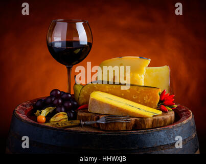 Morbier, Emmentaler Käse und Gouda mit Glas Rotwein im rustikalen Stillleben Stockfoto