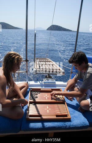 Teenager-Mädchen und Jungen spielen Backgammon auf der Rückseite ein Boot an der Mittelmeerküste der Türkei. Stockfoto