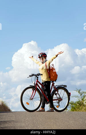 Frau Radfahrer stehen mit dem Fahrrad auf der Straße Horizont und die Hände zum Himmel emporgehoben. Stockfoto