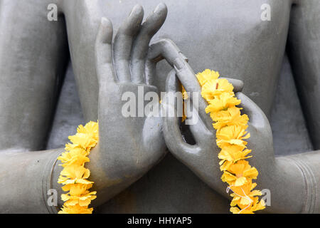 Die Details der Statue des Buddha in Meditation Position. Hände, die meditieren Buddha mit einem Kranz von gelben Blüten. Stockfoto