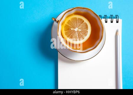 Quadratische Notizblock auf Federn mit weißen Kraftpapier, Bleistift, Tasse Tee sind auf blauem Hintergrund. Stockfoto