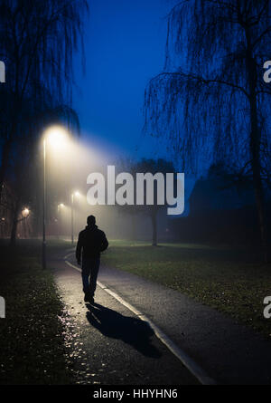 Eine einsame Gestalt zu Fuß entlang eines Pfades durch Straßenlaternen beleuchtet Stockfoto