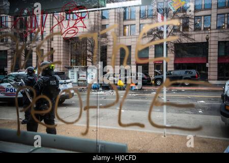 Demonstranten, die bei der Amtseinführung von Präsident Donald Trump in Washington DC. Szene einer Bushaltestelle Sitzecke mit Graffiti, die lautet: "Wir, das Volk' und eine ausgebrannte Limousinen im Hintergrund, Polizei Patrouille der Straße. Stockfoto