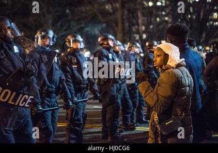 Demonstranten, die bei der Amtseinführung von Präsident Donald Trump in Washington DC. Eine junge schwarze Frau und ihren Partner stand trotzig, mit einer Faust fo Solidarität angehoben, vor der Polizei in taktisches Gang gekleidet. Stockfoto