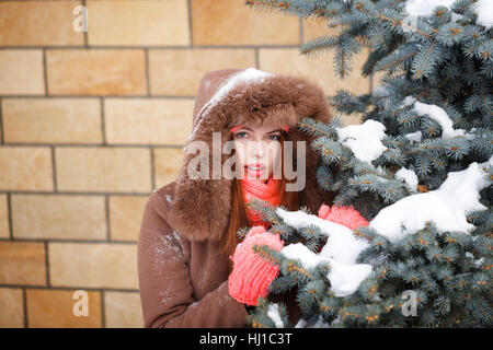 Cute Teen Mädchen in rosa gestrickte Handschuhe, Mützen und Schals, Spaziergänge mit Kapuze Fell Jacke Winter im Park. Sie steht neben dem Weihnachtsbaum. Stockfoto