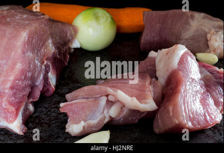 Gemeinsame rohes Schweinefleisch, Zwiebeln, Knoblauch und Karotten auf dunklen Stein Hintergrund Stockfoto