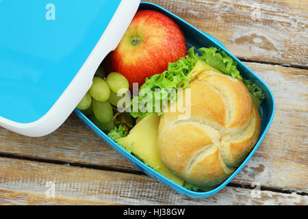 Offenen Lunch-Box mit Brötchen mit Käse und Salat, roten Apfel und Trauben auf rustikalen Holz Stockfoto