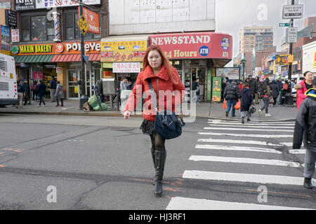 Ein asiatisch-amerikanische Frau in einem kurzen Rock und hellen Mantel überqueren Roosevelt Ave in Chinatown, Flushing, Queens, New York City. Stockfoto