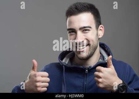 Aufgeregt, fröhliche junge Mann trägt Hoodie mit Daumen hoch Geste Stockfoto