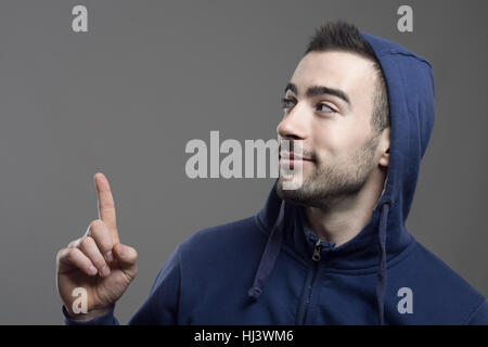 Glücklich lächelnd junger Mann Hoodie wegsehen und Finger oben tragen. Stockfoto