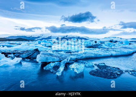 Eisberge entlang der Ufer der Jökulsárlón Gletscherlagune Verlauf einer blauen bewölkten Tag bewegungslos während umrahmt von einer kalten Ozeanwasser. Stockfoto