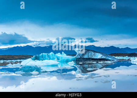 Eisberge entlang der Ufer der Jökulsárlón Gletscherlagune Verlauf einer blauen bewölkten Tag bewegungslos während umrahmt von einer kalten Ozeanwasser. Stockfoto