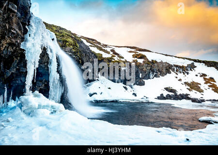 Ein kalten verschneiter Wasserfall im Hochland von Island umrahmt von Pastell Himmel und zerklüftete Gelände bietet landschaftlich Inbegriff der gefrorenen Wildnis Stockfoto