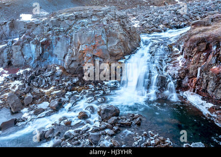 Ein Wasserfall in Island Kaskaden hinunter die Seite eines zerklüfteten Berges in einem Naturpool Stockfoto