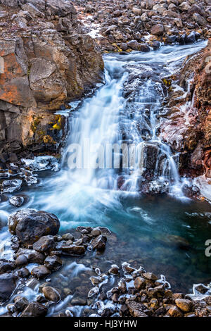 Ein Wasserfall in Island Kaskaden hinunter die Seite eines zerklüfteten Berges in einem Naturpool Stockfoto