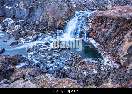 Ein Wasserfall in Island Kaskaden hinunter die Seite eines zerklüfteten Berges in einem Naturpool Stockfoto