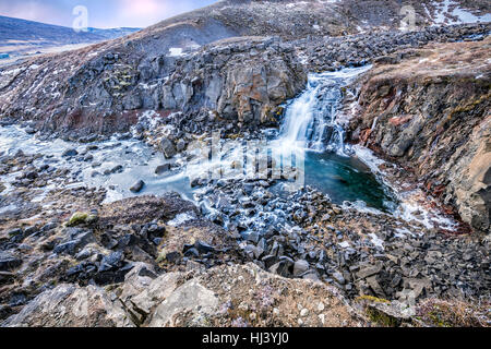 Ein Wasserfall in Island Kaskaden hinunter die Seite eines zerklüfteten Berges in einem Naturpool Stockfoto