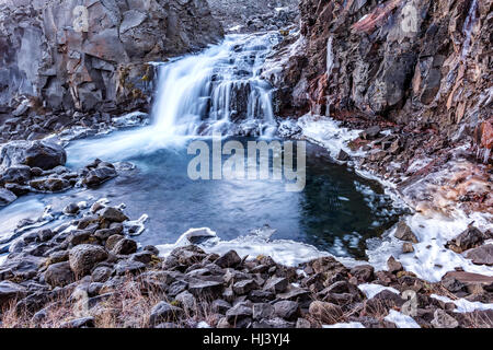 Ein Wasserfall in Island Kaskaden hinunter die Seite eines zerklüfteten Berges in einem Naturpool Stockfoto