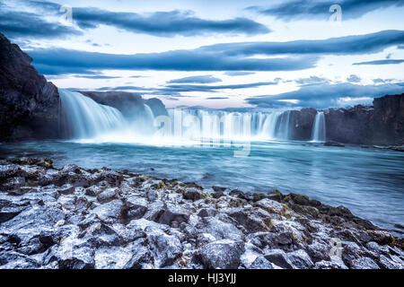 Godafoss Wasserfall bei Sonnenaufgang zeigt das Wasser in Strömen über die Kante und kicking eine neblige Wolke über dem Wasser mit Schnee bedeckt die Klippen. Stockfoto