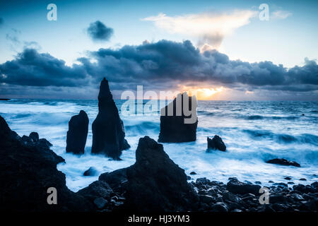 Ein einsamen Strand in Island zeigt scharfe felsigen Riffen hervorstehenden 20 Fuß aus dem seichten Wasser während eines Sonnenuntergangs. Stockfoto