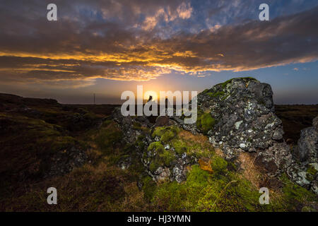 Sonnenuntergang über eine am Meer gelegene Marschland zeigt eine sehr launische, dunkle Landschaft umrahmt von Felsen und vegetation Stockfoto