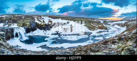 Ein kalten verschneiter Wasserfall im Hochland von Island umrahmt von Pastell Himmel und zerklüftete Gelände bietet landschaftlich Inbegriff der gefrorenen Wildnis Stockfoto