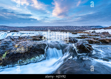 Godafoss Wasserfall bei Sonnenaufgang zeigt das Wasser in Strömen über die Kante und kicking eine neblige Wolke über dem Wasser mit Schnee bedeckt die Klippen. Stockfoto