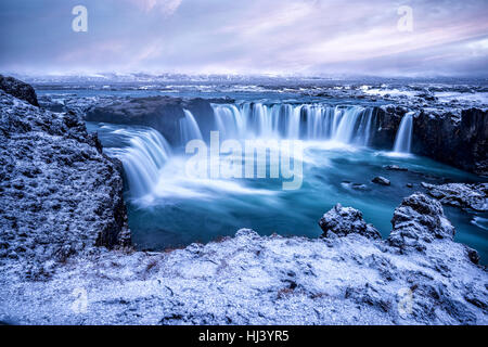 Godafoss Wasserfall bei Sonnenaufgang zeigt das Wasser in Strömen über die Kante und kicking eine neblige Wolke über dem Wasser mit Schnee bedeckt die Klippen. Stockfoto