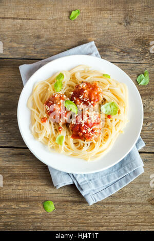 Spaghetti Nudeln mit Fleischbällchen, Tomatensauce, geriebenem Parmesan und frischem Basilikum - gesunde hausgemachte italienische Pasta auf rustikalen hölzernen Hintergrund mit Stockfoto