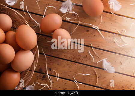 Frisch gepflückt Eiern im Weidenkorb auf Holztisch mit Stroh und Federn. Ansicht von oben. Horizontale Komposition. Stockfoto